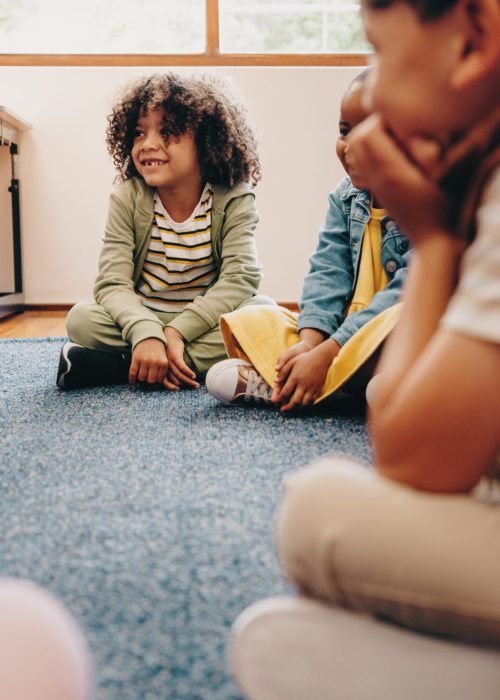 Group of children sitting in a circle in a classroom. Boys and girls enjoy learning in school, they listen their educator during a lesson. Kids schooling together in an early child development centre.